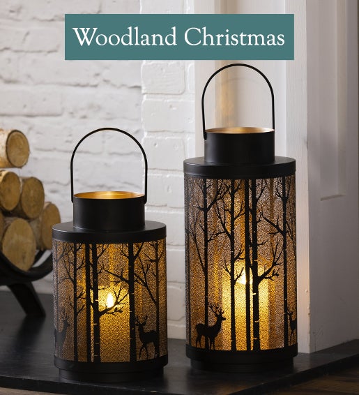 A pair of glowing lanterns with cut-out forest scenes. Shop Woodland Christmas. 