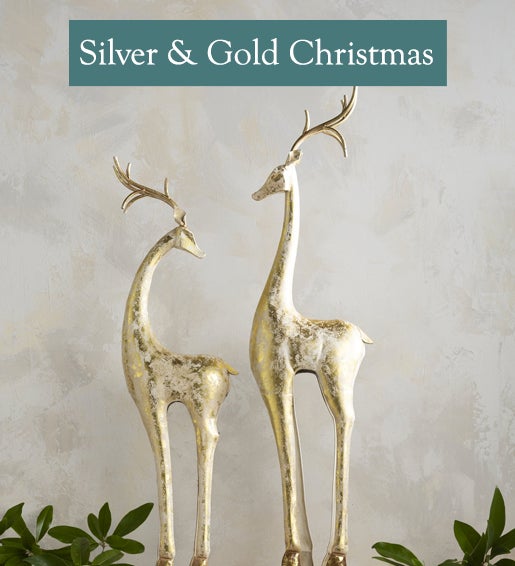 A pair of slender golden reindeer statues stand on a mantel. Shop Silver & Gold Christmas.