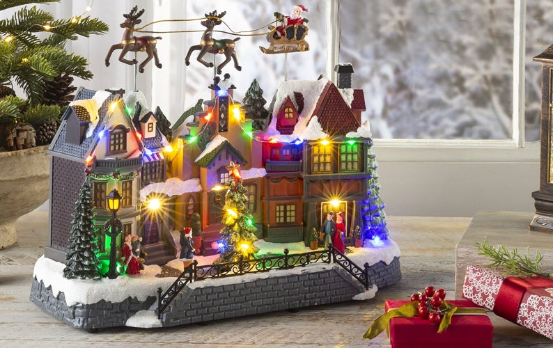 A charming lighted Christmas village with Santa flying above it sits on a table